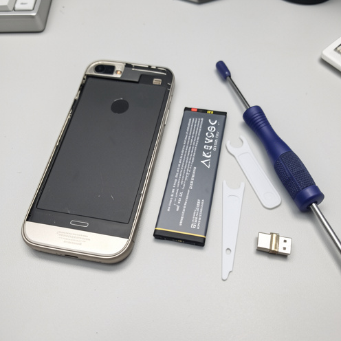 Smartphone ancien ouvert avec batterie de remplacement et outils de réparation disposés sur un établi.