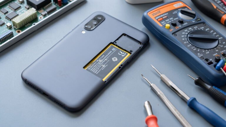 Smartphone ouvert sur un établi, avec sa batterie visible et des outils de diagnostic à côté.