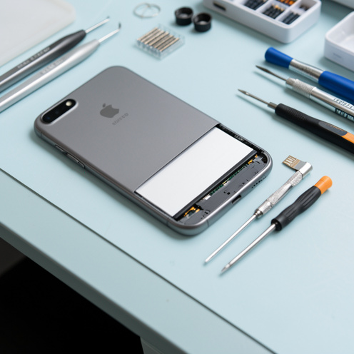 Smartphone ouvert avec sa batterie visible, entouré d’outils de réparation sur un établi clair.