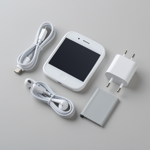 Petit smartphone blanc du début des années 2010 présenté avec son chargeur, son adaptateur secteur, ses écouteurs et sa batterie amovible sur une table claire.