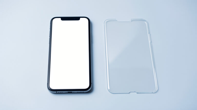 Un smartphone posé à côté d’un verre trempé rigide et d’un film hydrogel transparent pour comparer les protections d’écran.